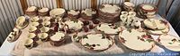 Wide view of the entire Franciscan Apple dinnerware collection arranged on a table showing plates, bowls, platters, coasters, cups, creamer, and sugar dish.