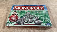 Full box view showing Monopoly branding, new token lineup text, and tokens like donkey, top hat, rubber duck and robot on cover.