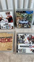 Four PS3 game cases arranged on carpet: NCAA Football 09, The Shoot, Tony Hawk Ride, and Madden NFL 10 showing front covers.