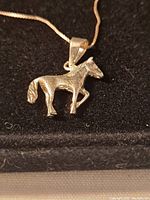 Close-up of the horse pendant on the chain showing detail, texture, and stamp mark.