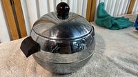 Side view showing the spherical metal hot and cold server with black knob and handle on a towel
