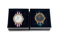 Two wooden framed watches displayed side by side in black textile boxes. One watch has a white face with red, white, and blue striped fabric strap; the other has a black face with green and blue striped fabric strap.