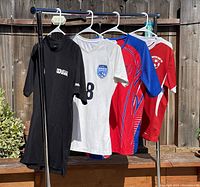 Four football club jerseys and tops hanging on rack outside in sunlight