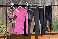View of all six activewear pieces on hangers on a clothing rack outside.