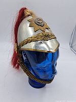 Side view of the silver dome helmet with attached brass star badge and red plume.