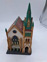 Front side view showing detailed green steeple, stained glass window, and textured brown roof.