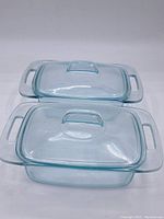 Two covered rectangular glass casserole dishes stacked, showing clear blue-tinted glass with handles and fitted lids.