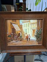 Framed oil painting showing street scene with couple walking on cobblestone street in Tuscany, Italy