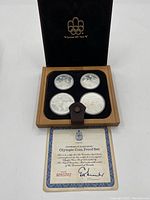 Overall view: wooden case open showing four coins and certificate.