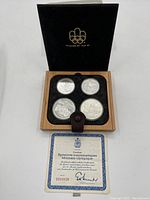 Wooden presentation case open showing four silver coins in black felt insert and certificate