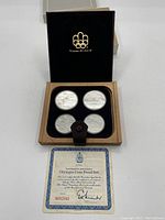 Wooden presentation case open showing four silver proof coins and certificate of authenticity