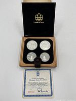 Opened wooden presentation box with four silver coins in acrylic capsules and certificate laid in front