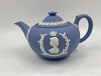 Side angle view of blue jasperware teapot showing the white relief profile of Queen Elizabeth II with crown and surrounding laurel wreath.
