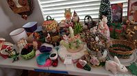 Table filled with holiday decor items including ceramic egg plate with bunnies, pumpkin bowls, woven baskets, and small decorative figures.