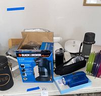 Photo showing a Black & Decker 5-Cup Coffeemaker in its box, a coffee canister, white George Foreman grill, GT Express cooker, thermos, and a flashlight.