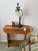 Wide image showing wood table with heart cutouts, black metal & glass lamp, and small furry figurine, plus framed art leaning nearby.
