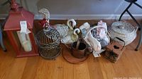 Lot displayed on floor includes large red lantern, metal birdcage with bird topper, plush swan figures, small copper bucket, small metal lantern, slippers, and a woven wicker basket.