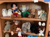 Full view of wooden shelf holding various stuffed animals including Pinocchio, owls, monkey, elephants, dog, fox, lamb, and doll.