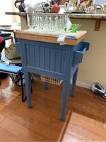Blue portable kitchen island with wood top, showing front and side paneling, towel rack, and wire basket storage