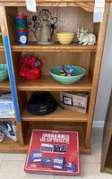 Shelf with red and blue Santa Claus buckets, metal angel candle holder, yellow bowl, white rabbit figurines, red and green bowls with decorations, black radio, digital photo frame box, and boxed Electric Jeopardy game.