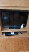Sony Bravia television and Sony DVD player set up in wooden entertainment unit on hardwood floor.