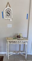 Full view of wooden entry table with candle, photo frame, small dish on top, and wall hanging above on the wall