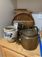 Full view of wooden churn, copper kettle, and ceramic crock on wooden surface