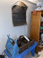 Front view of wooden blue birdhouse attached to blue bench with wooden carry case on top showing irons inside