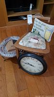 Wooden vanity chair with floral seat cushion and carved backrest, large round wall clock, oval mirror with decorative frame, and decorative pillow all arranged on wood floor