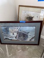 Two framed wolf prints with one showing two wolves behind branches and the other showing a single wolf in snow.