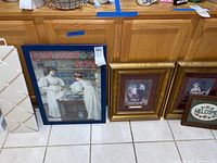Large Sunlight Soap vintage advertising poster with two women in white clothing, framed in blue, and smaller gold framed prints next to it on the floor against cabinets
