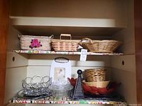 Shelf with woven baskets, clear glass bowls, metal fruit stand, metal trays, grater, and wooden cutting board.