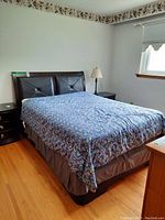 View of wood framed bed with cushioned wooden headboard and floral bedspread in bedroom setting.