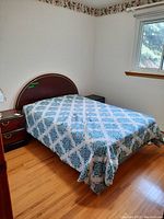 Bed with metal frame and wooden curved headboard along a wall with window, covered in blue patterned bedding.