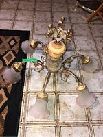 View of the chandelier showing the 5 curved arms with ribbed frosted bell-shaped glass shades and central ceramic base with cherub figurines.