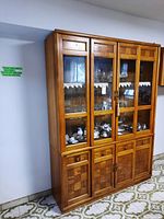 Front view of the wood china cabinet showing the two framed glass doors on top, two drawers, and two lower wood doors with paneled design. The cabinet is set against a wall with patterned flooring visible.