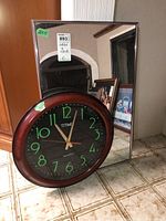 Photo showing rectangular mirror standing behind round clock on tiled floor. Mirror size approximately 28x18 inches.