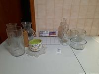 Photo showing a group of glassware and ceramic items on a countertop against tiled wall including vases, glass jars with stoppers, a ceramic bowl, glass bowls, a corked jar, and the coated metal under-shelf rack.
