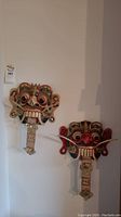 Both Balinese Rangda masks hung on a white wall side by side, showcasing full front view, highlighting size and symmetry.