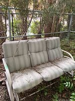 Front view of the 3 seater bench glider swing showing the white metal frame and striped cushions with outdoor debris.