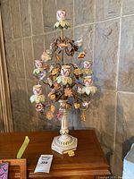 Full view of candelabra showcasing metal branches with ceramic flowers, multiple candle holders and hexagonal base with painted leaves.