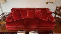 Front view of red velvet three-seater sofa with five matching cushions set against a wall.