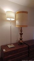 Front view of the two lamps side by side on wooden furniture, showing size and style contrast