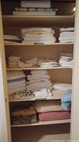 Closet shelf with assorted folded linens including table linens, bedding, blankets, and towels of various sizes and colors.