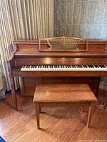 Full view of Mason & Risch upright piano with bench placed in front. Shows wood finish and detached book stand resting on piano.