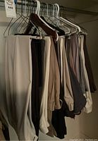 Side view of eight men's dress pants hung on hangers in various colors from beige to dark brown and black.