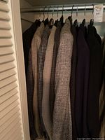 Photo showing seven men's suit jackets hanging on hangers, various patterns and neutral colors.