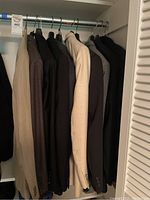 Seven men's suit jackets hung on a rod, showing variety in color and fabric.