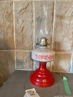 Full view of the vintage oil lantern showing the red base with floral painted design and clear glass chimney.