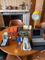Full view of assorted vintage and electronic items on round wooden table showing Sony Clie, yellow desk lamp, pins, hair dryer, clock, and other accessories.
